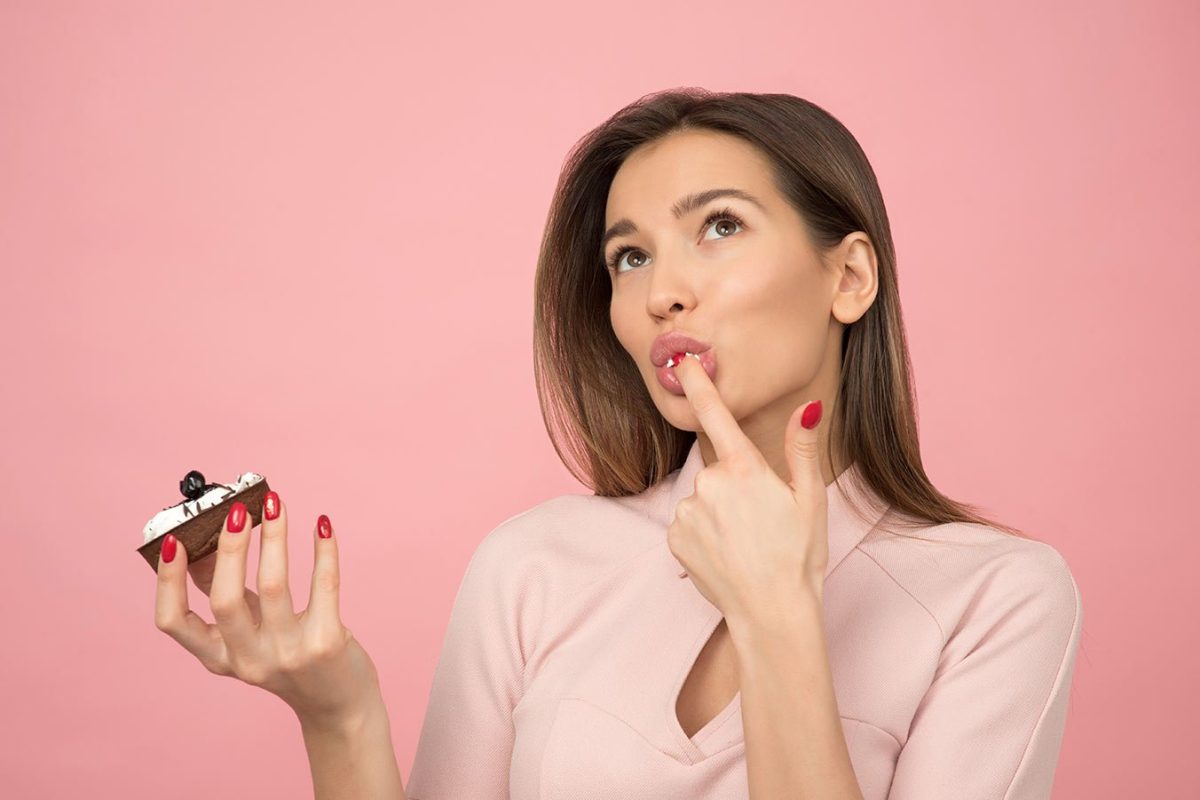 woman-eating-cupcake-while-standing-near-pink-background-1036621